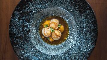 A round black plate with a speckled design, containing three scallops and a garnish, on a wooden surface.
