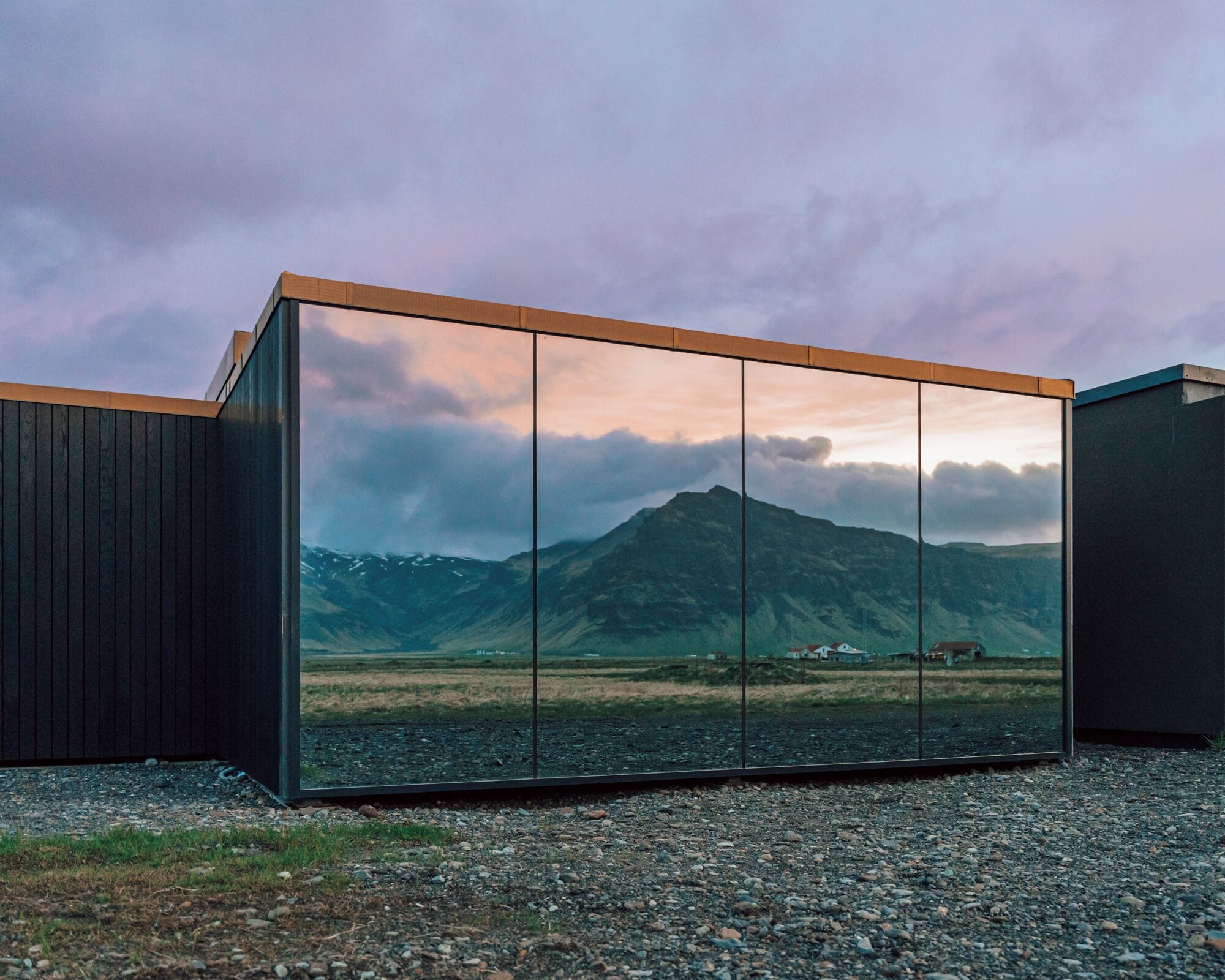 Un bâtiment moderne doté d’une grande façade vitrée qui reflète un paysage montagneux.