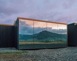 Un edificio moderno con un amplio frente de vidrio que refleja un paisaje montañoso.
