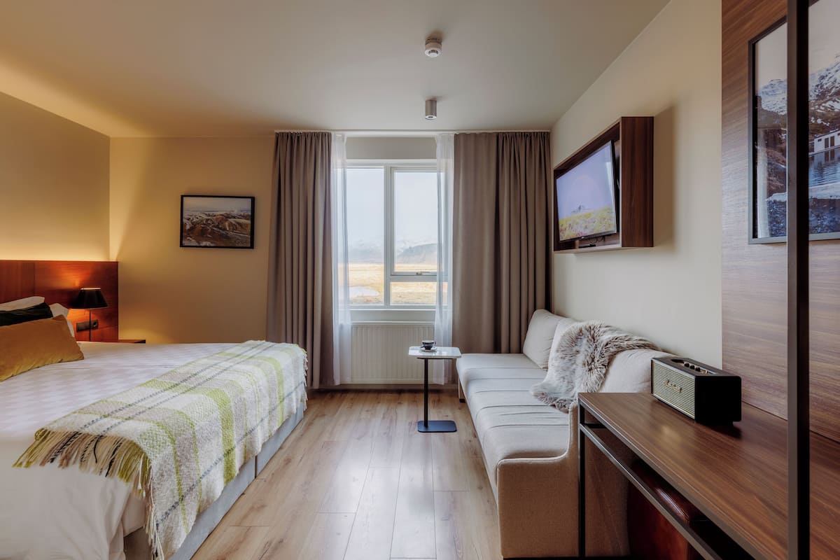 A hotel room with a bed, a sofa, a small table, a TV, and a window with curtains.