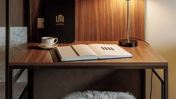 Un bureau en bois sur lequel se trouve un cadre avec une photo, une lampe noire, un carnet, une tasse et un livre noir avec l’inscription « UNI HOTEL ».