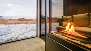 A modern interior with a glass wall, a sofa, and a fireplace. - UMI Hotel (Rangárþing eystra)