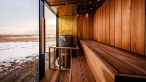 A wooden sauna with a bench and a stone container, overlooking a snowy landscape. - UMI Hotel (Rangárþing eystra)