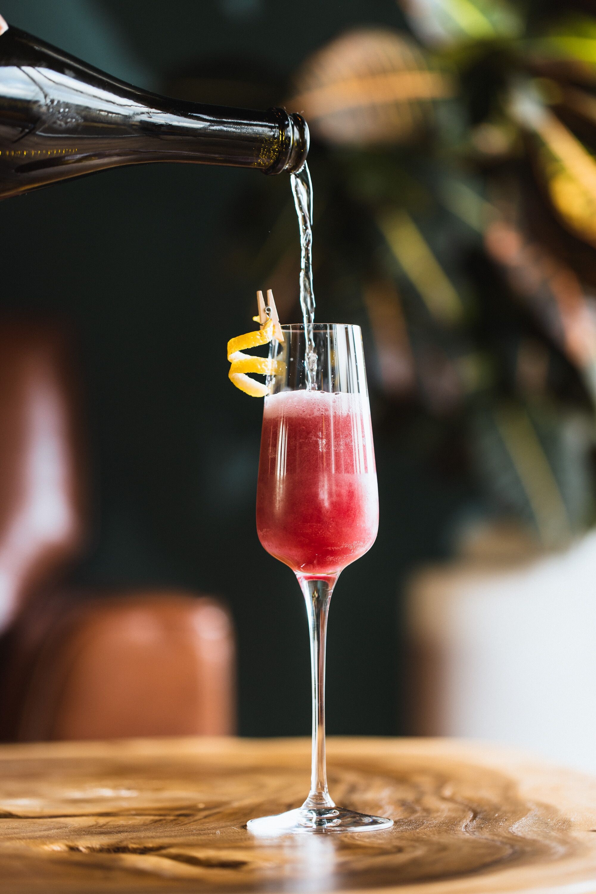 A cocktail being poured into a glass with a lemon twist garnish.