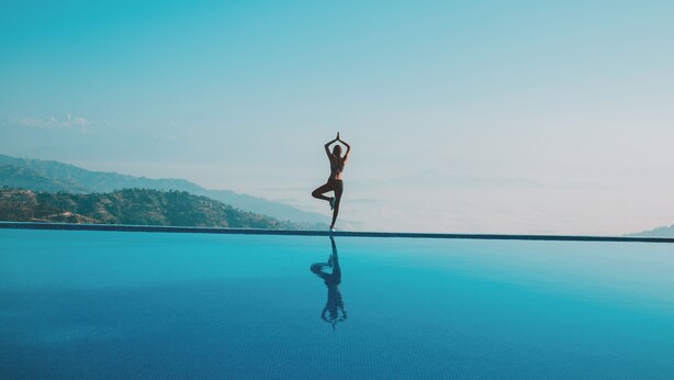 A person performing yoga on a reflective surface with a mountainous landscape in the background. - Hotel Himalayan Horizon (Dhulikhel)