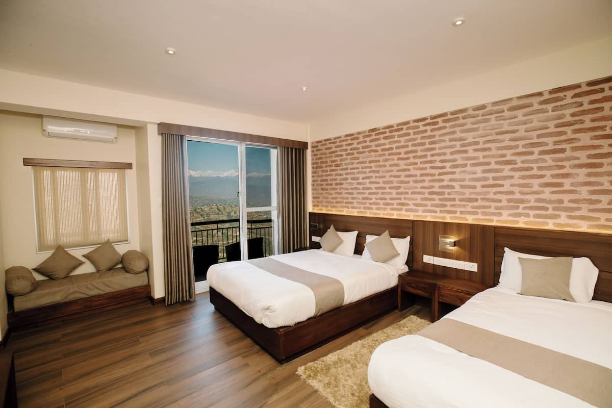 A hotel room with a large bed, a sofa, a view of the mountains, and a brick wall.