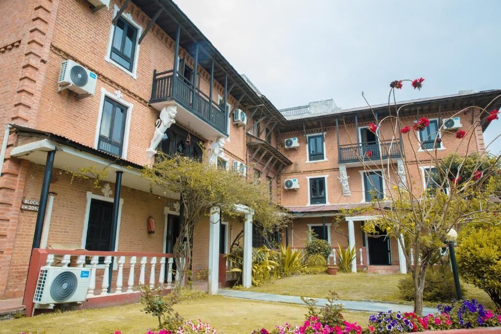 Un edificio de varios pisos de ladrillo con balcones, unidades de aire acondicionado y un jardín bien cuidado con flores de colores.
