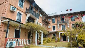 Un edificio de varios pisos de ladrillo con balcones, unidades de aire acondicionado y un jardín bien cuidado con flores de colores.