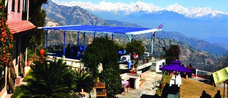 A view of a mountainous area with a blue-roofed structure, possibly a restaurant or cafe, surrounded by greenery and a small shrine.