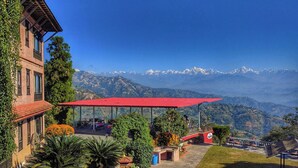 A building with a red roof, outdoor seating, and a mountain view. - Hotel Himalayan Horizon (Dhulikhel)