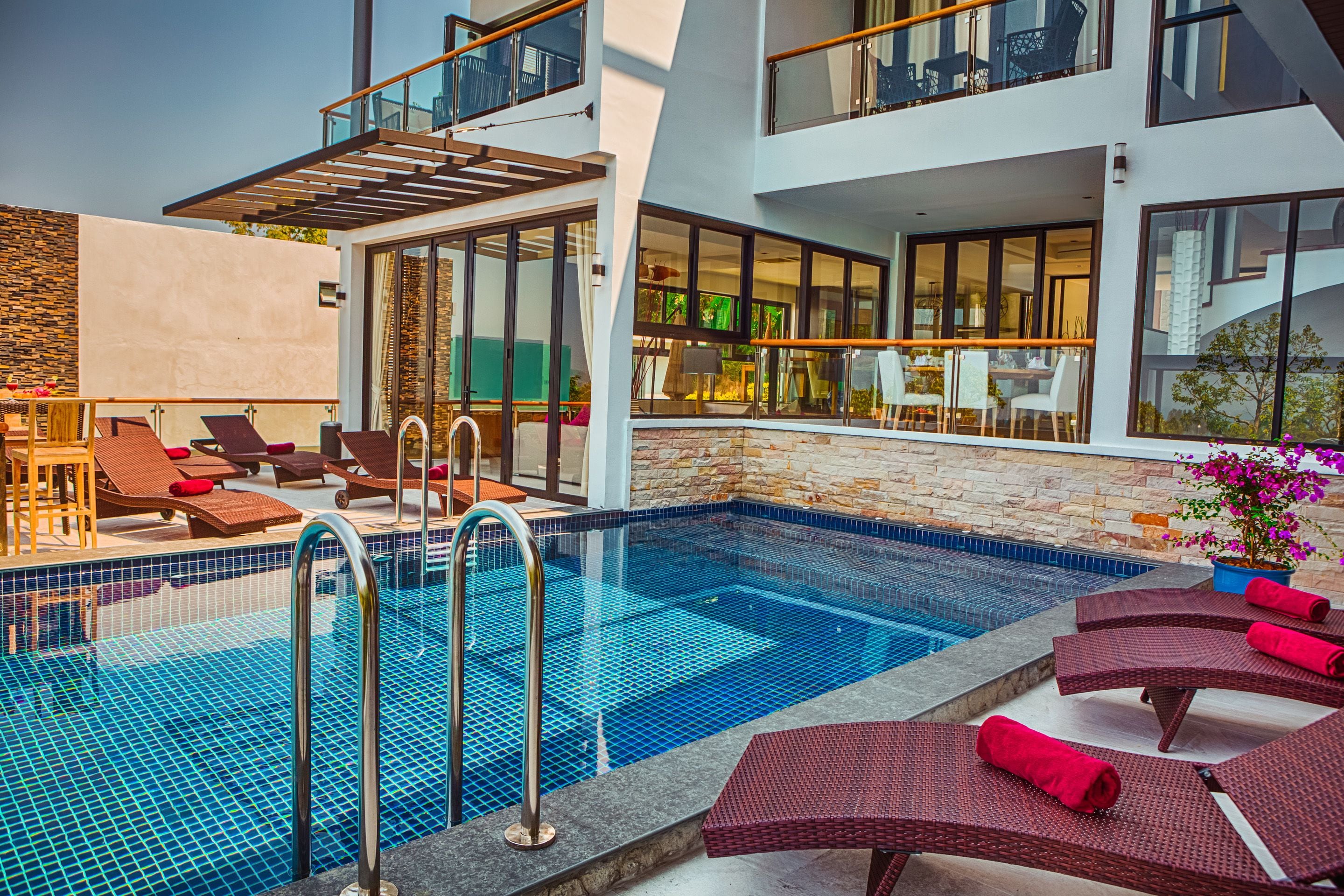 A modern pool area with lounge chairs, a glass balustrade, and a stone wall.
