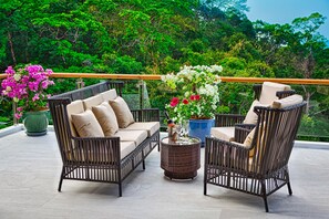 A balcony with wicker furniture, potted plants, and a glass railing overlooking a lush green landscape. - SHA Extra Plus Grand Villa Luxury Time (Choeng Thale)