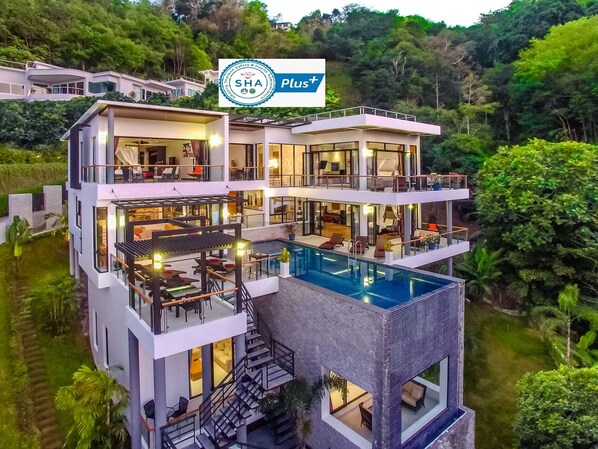 A modern multi-story building with a pool, balconies, and a sign indicating it is a SHA Plus hotel. - SHA Extra Plus Grand Villa Luxury Time (Choeng Thale)