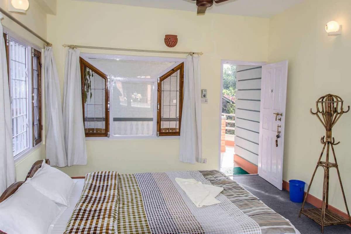 Une chambre à coucher avec un lit, une fenêtre avec des rideaux, un ventilateur de plafond et une porte donnant sur l’extérieur.