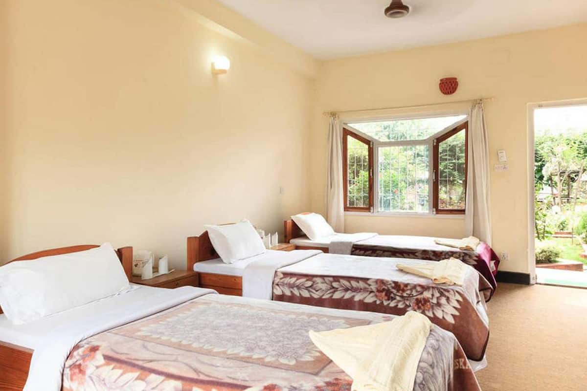Une chambre d’hôtel avec trois lits, une fenêtre avec des rideaux et une vue sur la verdure.