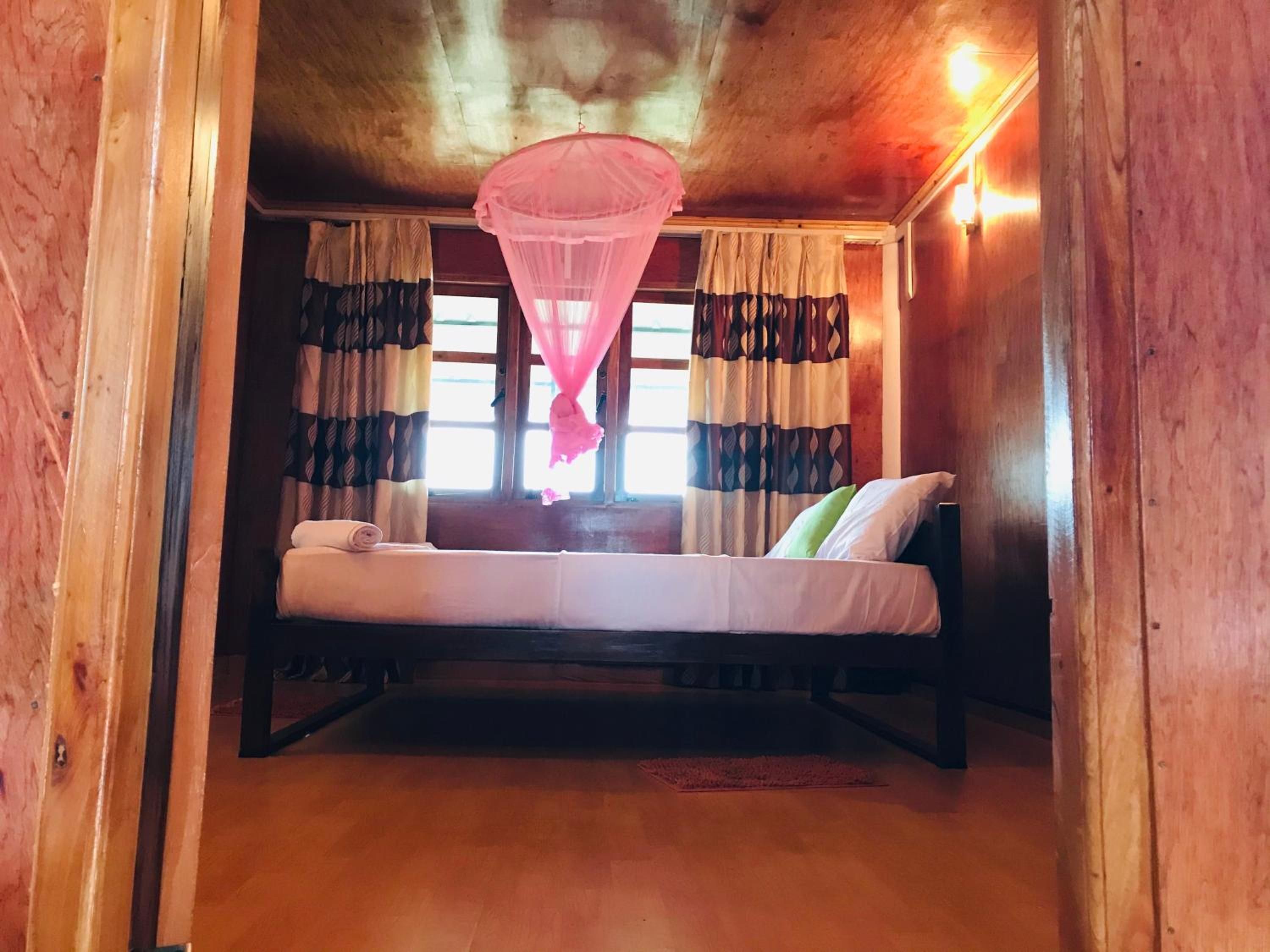 Una habitación con una cama, un ventanal con cortinas y una mosquitera colgante.