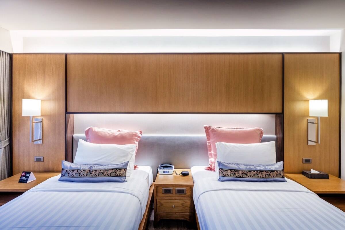Una habitación de hotel con dos camas, cada una con un almohadón y una mesita de noche con lámpara.