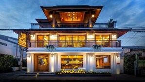 Un bâtiment à deux étages abritant un restaurant appelé « Tomkitti » au rez-de-chaussée, avec de grandes fenêtres et un balcon.