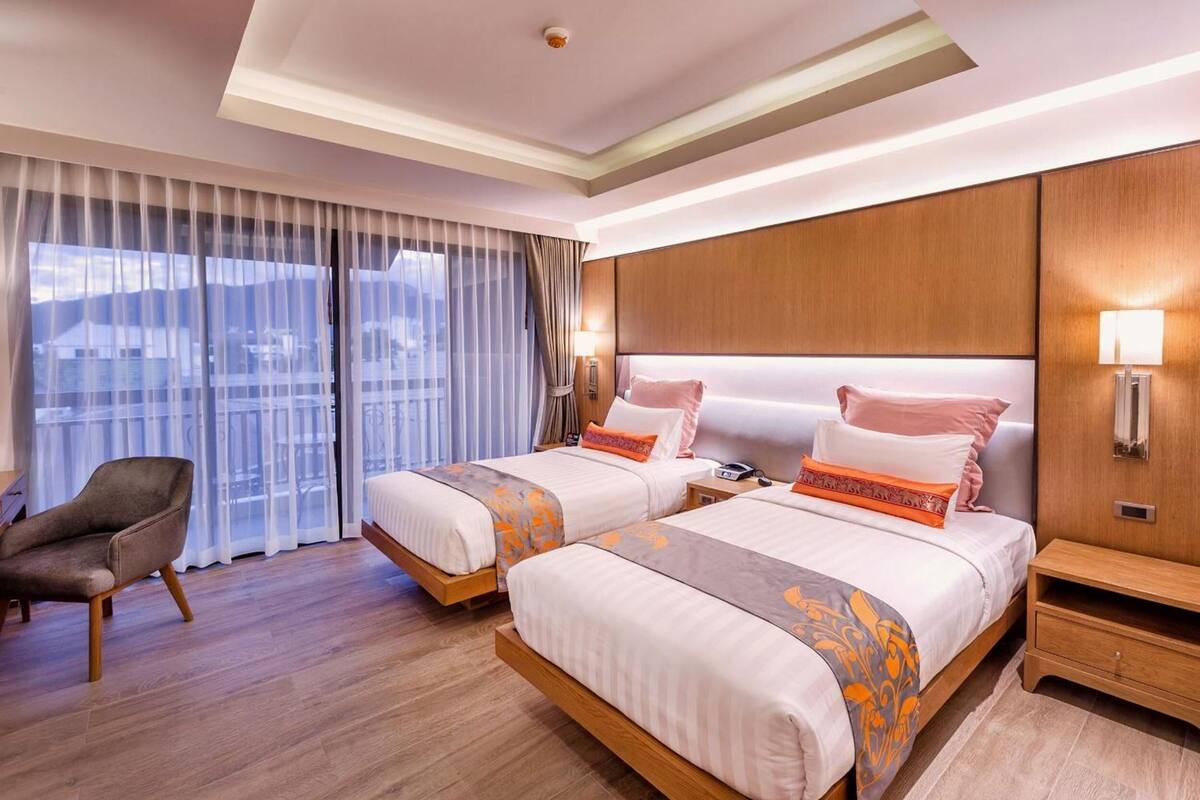 Habitación de hotel con dos camas, una silla, una mesita de noche y vistas a la ciudad.