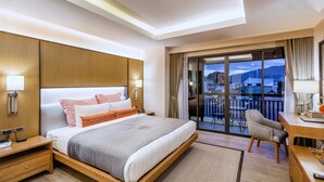Une chambre d’hôtel avec un grand lit, un bureau, une chaise et un balcon offrant une vue sur la ville et les montagnes.
