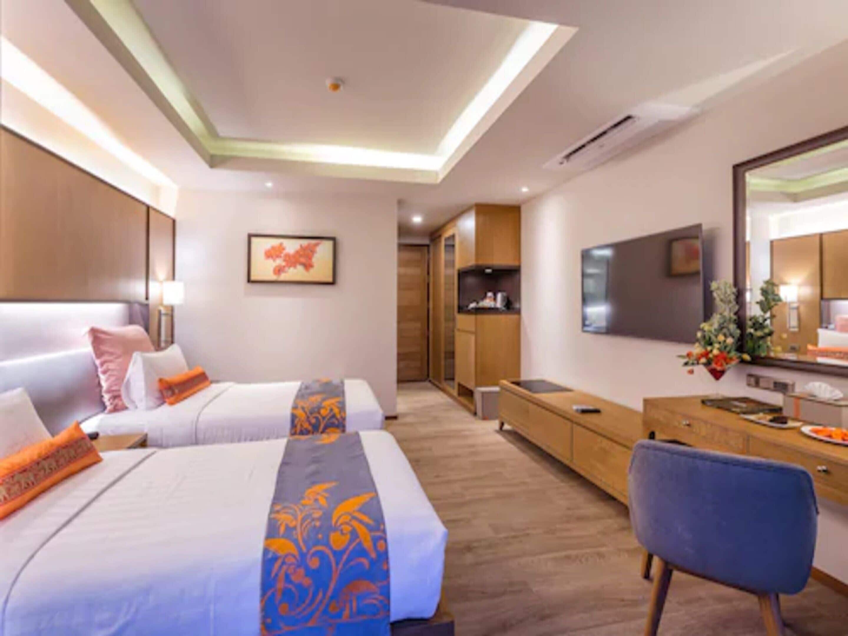 Ein modernes Hotelzimmer mit zwei Betten, einem Schreibtisch, einem Sessel, einem Fernseher und einem großen Spiegel.