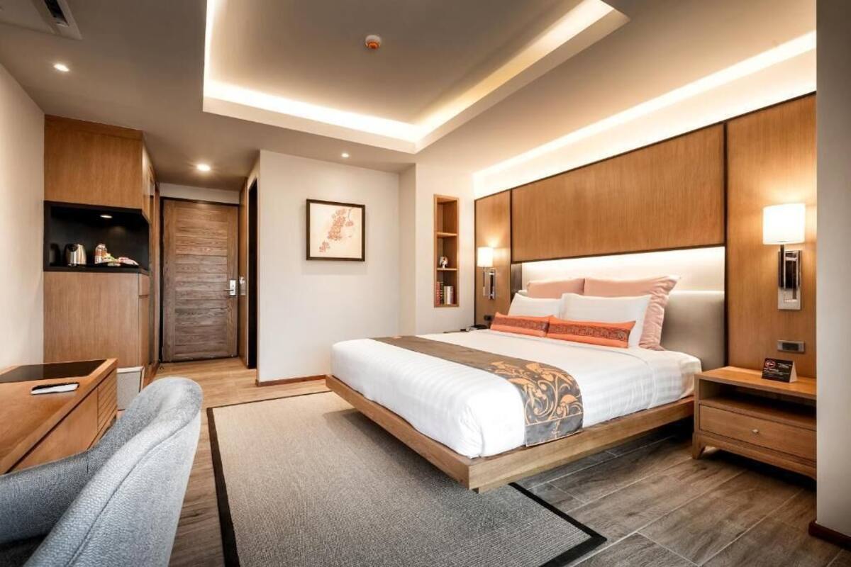 Una habitación de hotel moderna con una cama grande, cabecera de madera, mesitas de noche, un escritorio y un armario.