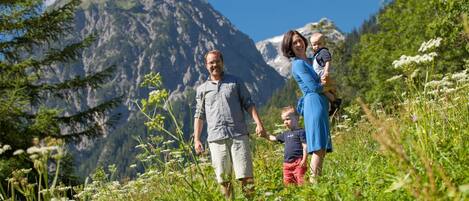 A family walking in a mountainous area with greenery and a clear sky.