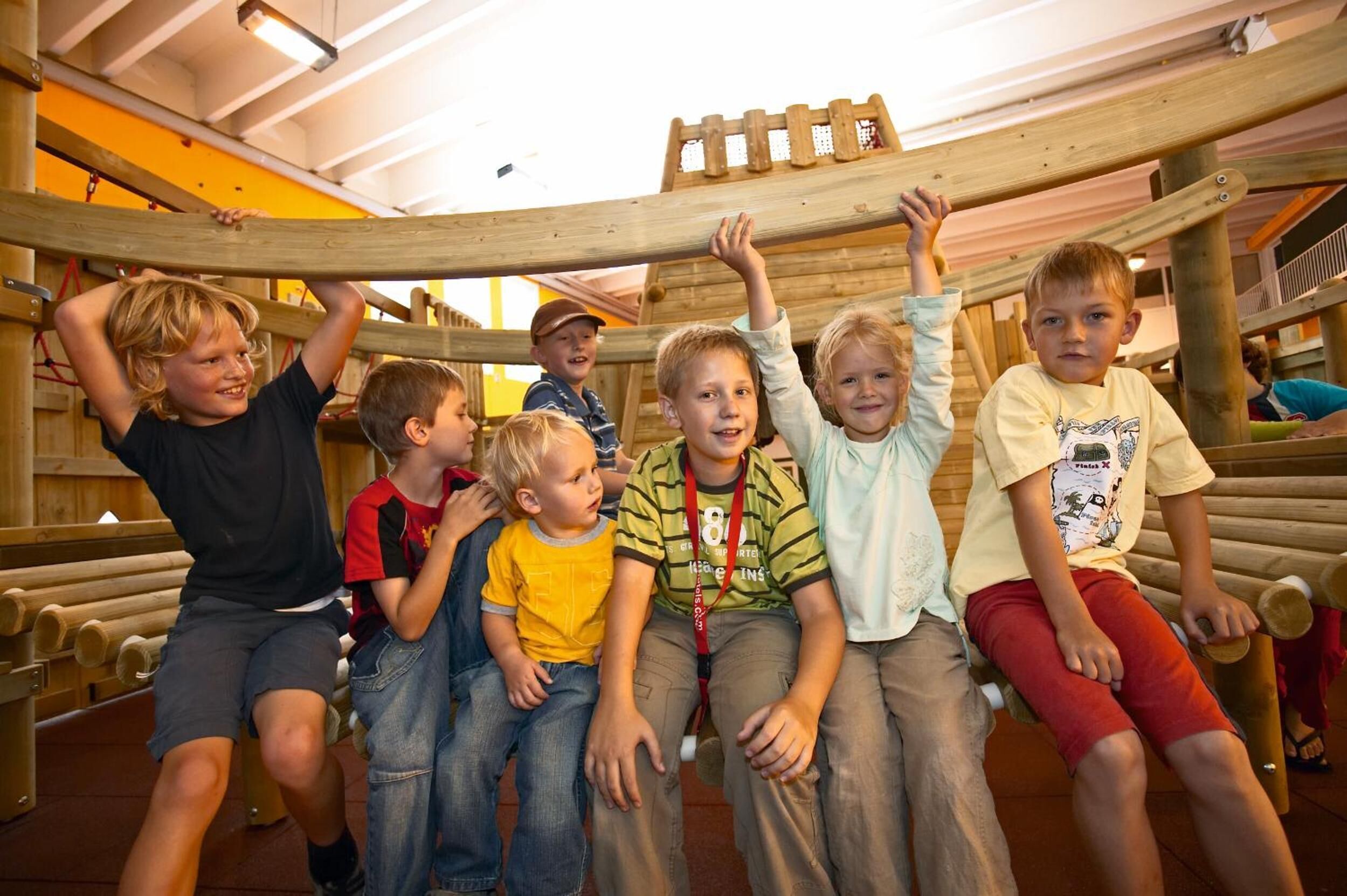 Children playing on a wooden play structure with a ladder and a platform.