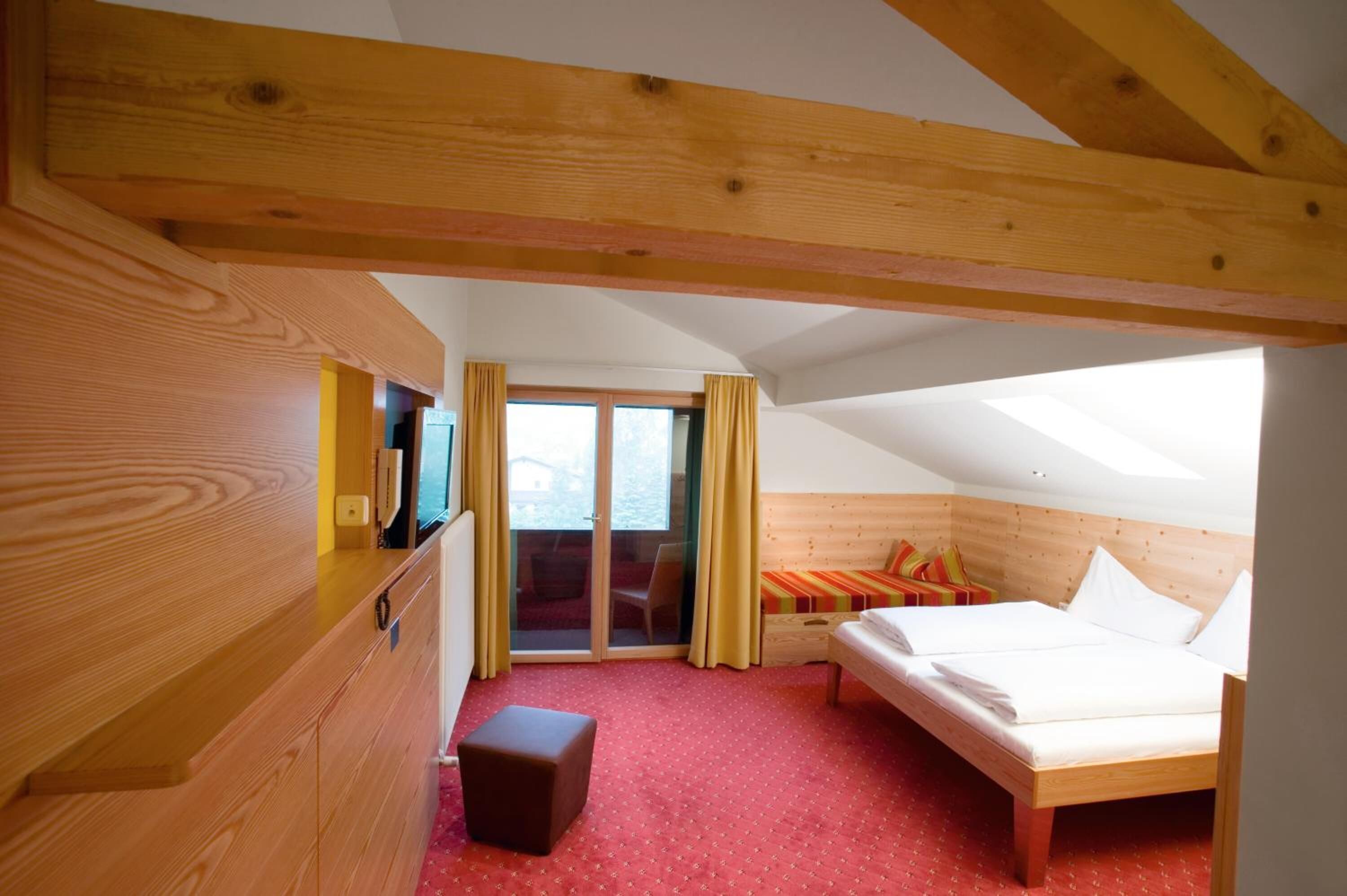 A bedroom with a wooden ceiling, a bed, a small table, a TV, and a sliding glass door leading to a balcony.