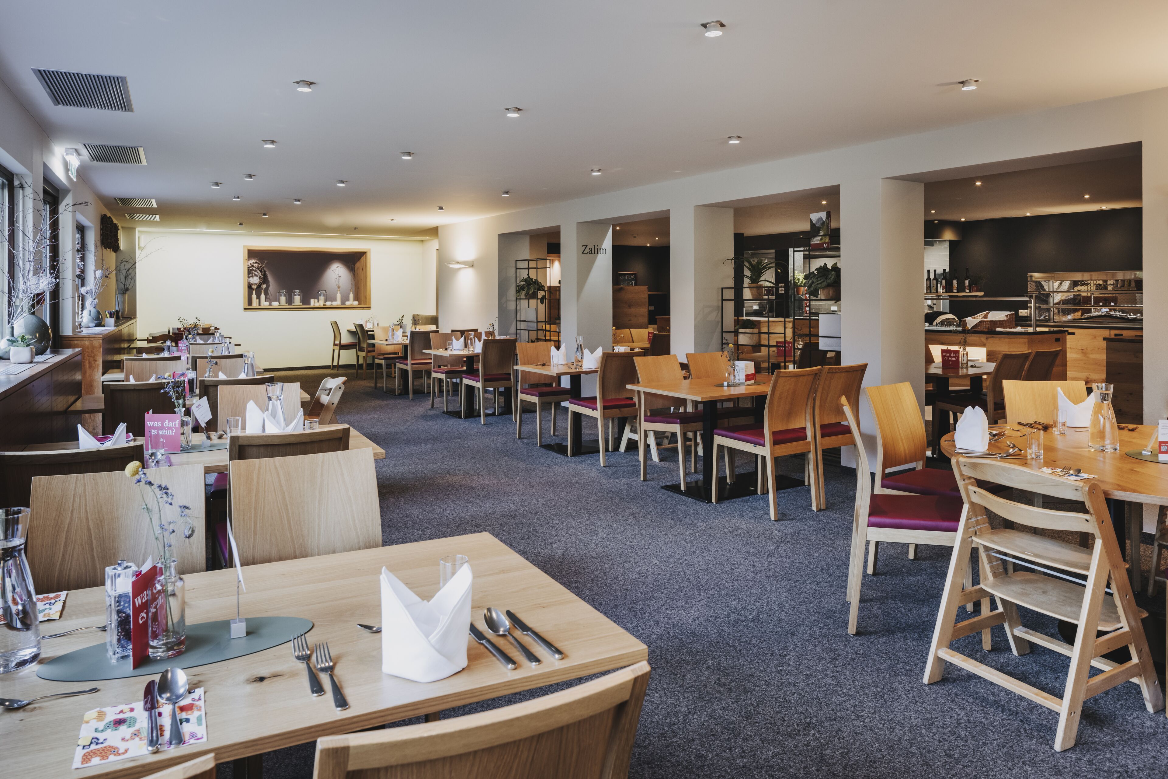 A spacious restaurant with multiple tables and chairs, a counter, and a display of food items.