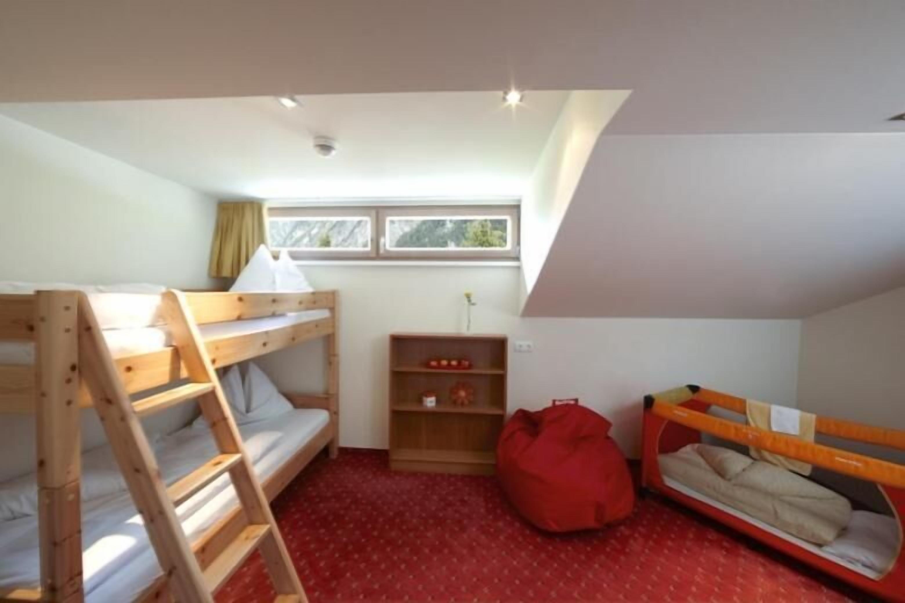 Ein kleiner Raum mit zwei Etagenbetten, einer Himmelsleiter, einem roten Sitzsack und einem Fenster mit Vorhängen.