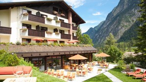 Um hotel com área externa para sentar, vista para montanhas e varandas com caixas de flores.