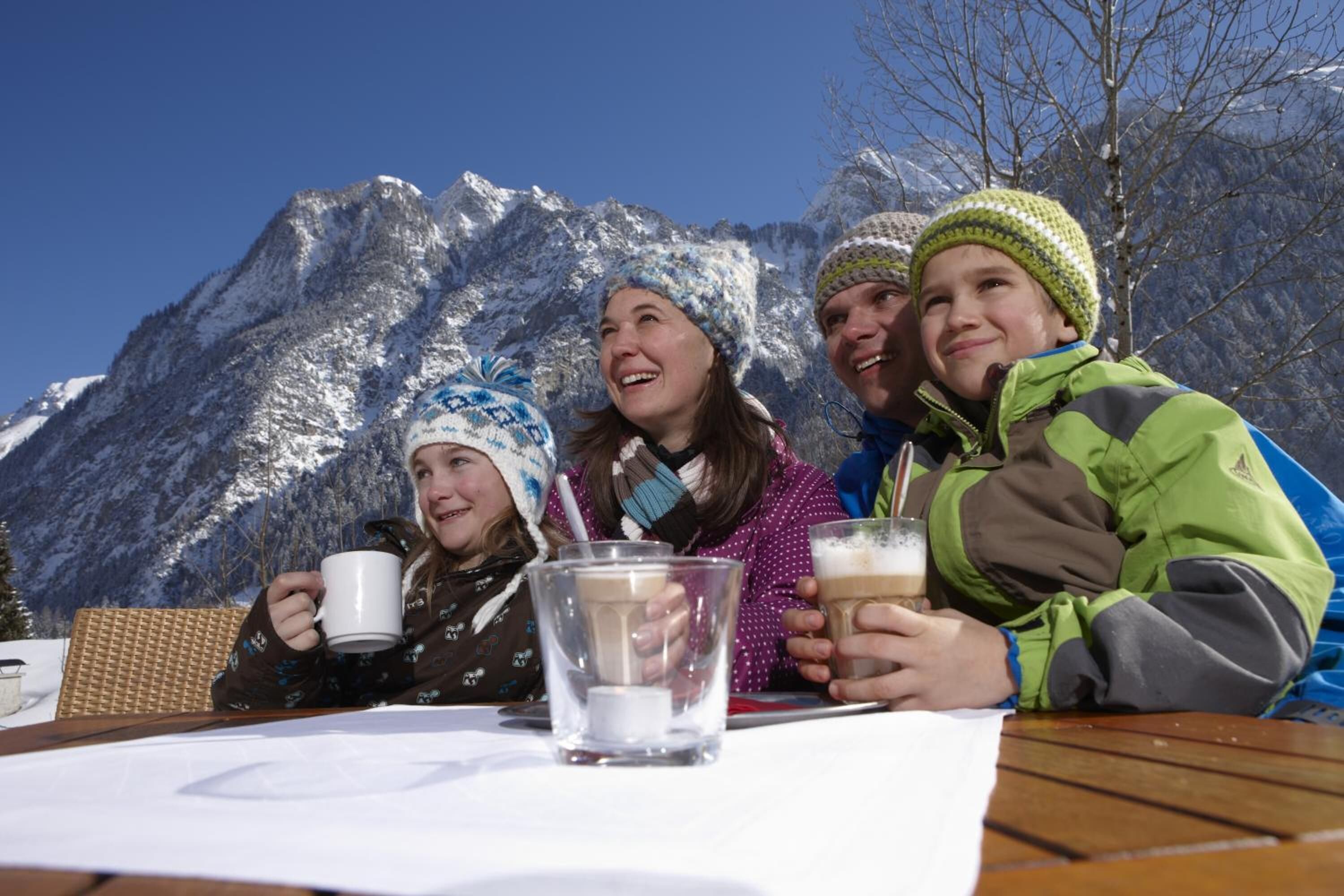 Un grupo de personas sentadas en una mesa de madera al aire libre, con montañas al fondo.