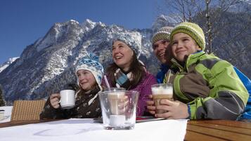 Un grupo de personas sentadas en una mesa de madera al aire libre, con montañas al fondo.