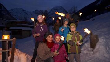 Eine Gruppe von Menschen hält Fackeln in einer verschneiten Winterlandschaft, im Hintergrund Berge.