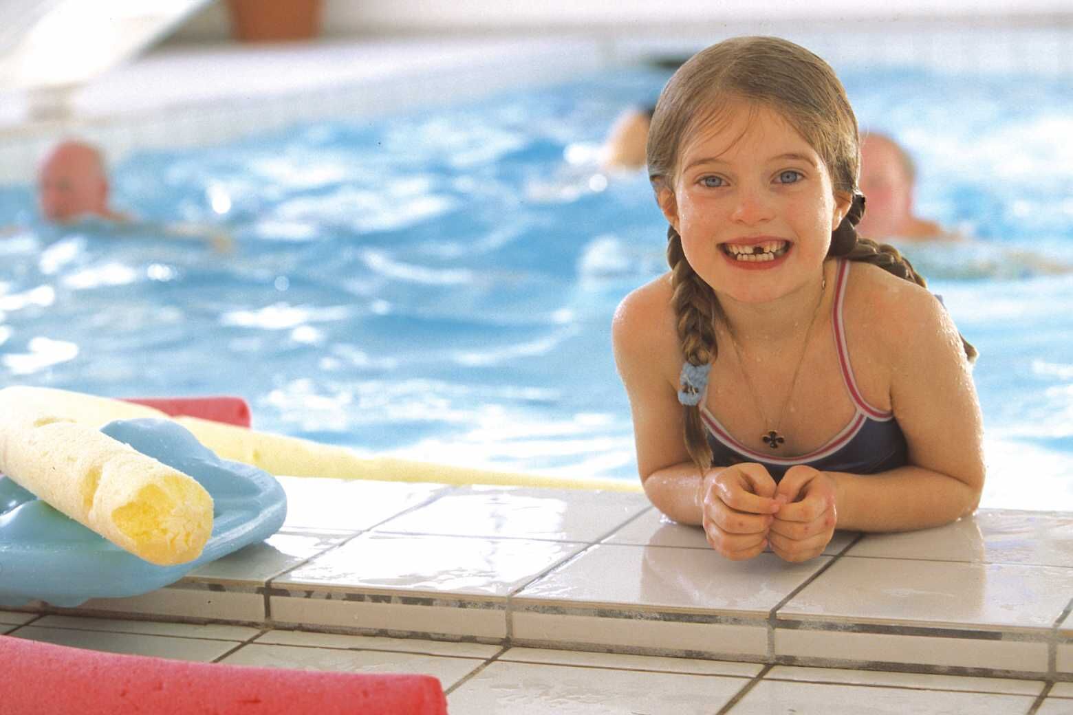 Un enfant dans une piscine, avec un flotteur en forme de long coussin et un autre flotteur.