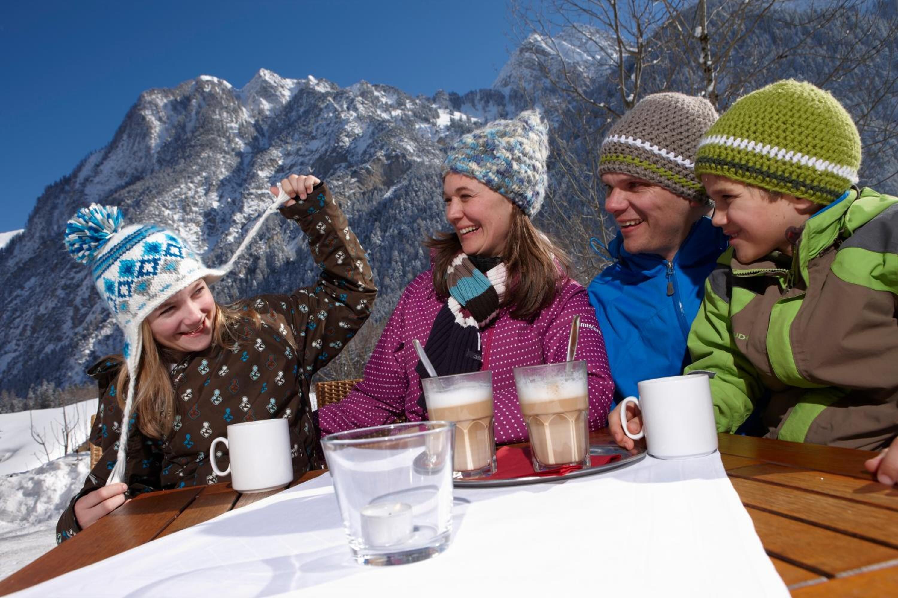 A group of people sitting at a wooden table outdoors with a mountain backdrop.