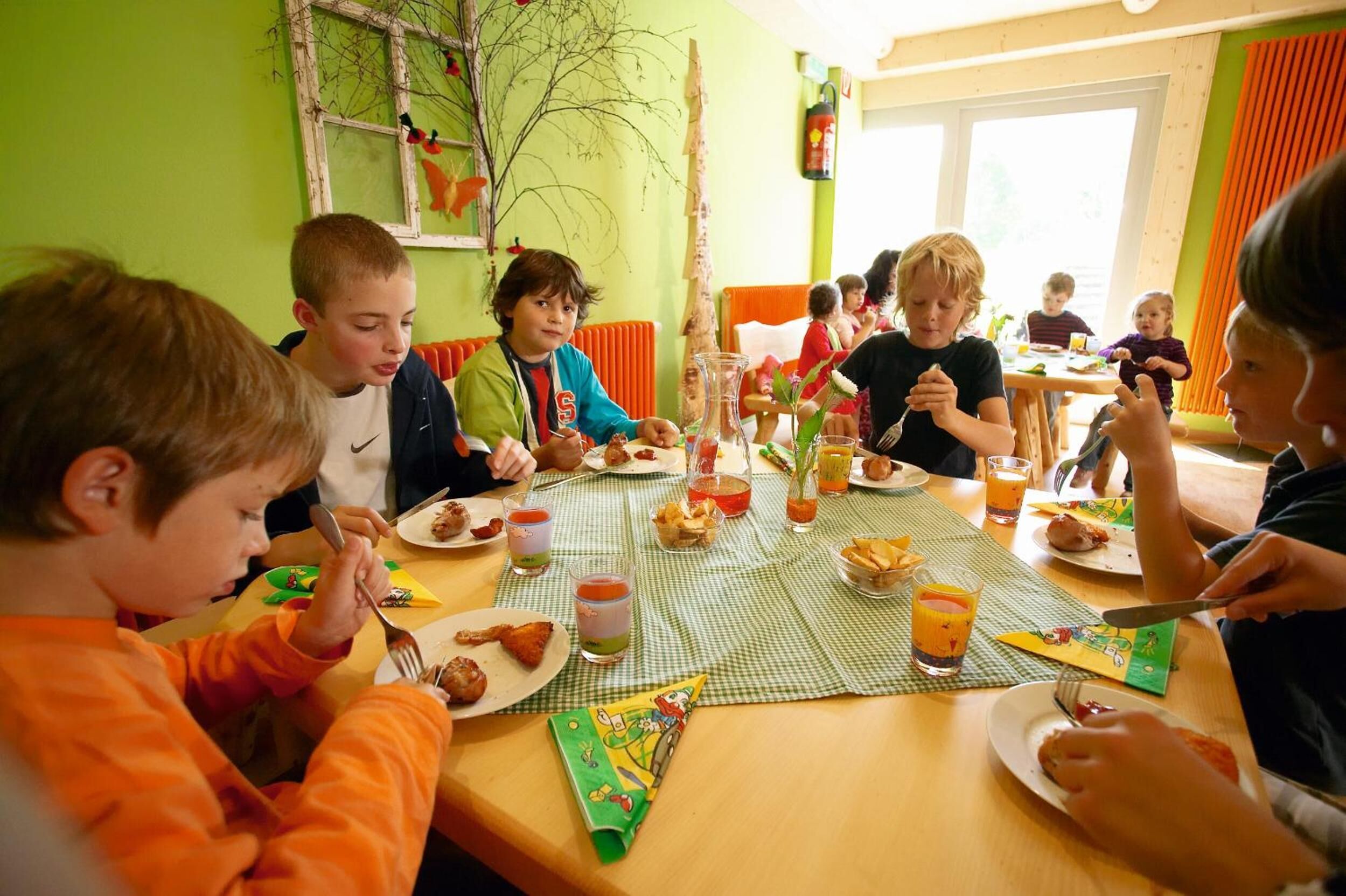 Un grupo de niños comiendo en una mesa con diversos alimentos y bebidas.