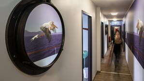 Un couloir orné d’un grand miroir rond qui reflète un oiseau en vol, d’une table d’appoint de couleur turquoise et d’une porte donnant sur une autre pièce.