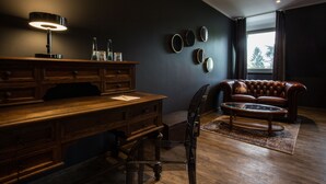 Une pièce aux couleurs sombres, avec un bureau en bois, un canapé en cuir et une table basse en verre.