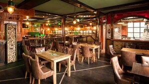 Un pub chaleureux avec des murs en bois, une cheminée, ainsi que de nombreuses tables et chaises.