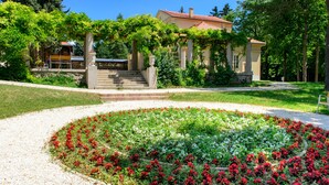 Un bâtiment avec un jardin à l’avant, un escalier menant à l’entrée et une pergola couverte de plantes grimpantes.