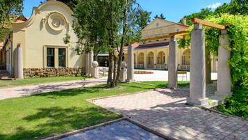 A courtyard with a paved walkway, stone columns, and a building with a yellow facade and arched windows.