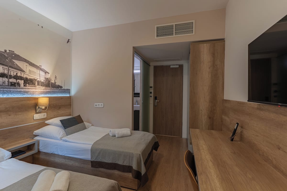 A hotel room with two beds, a desk, a TV, and a mural on the wall.