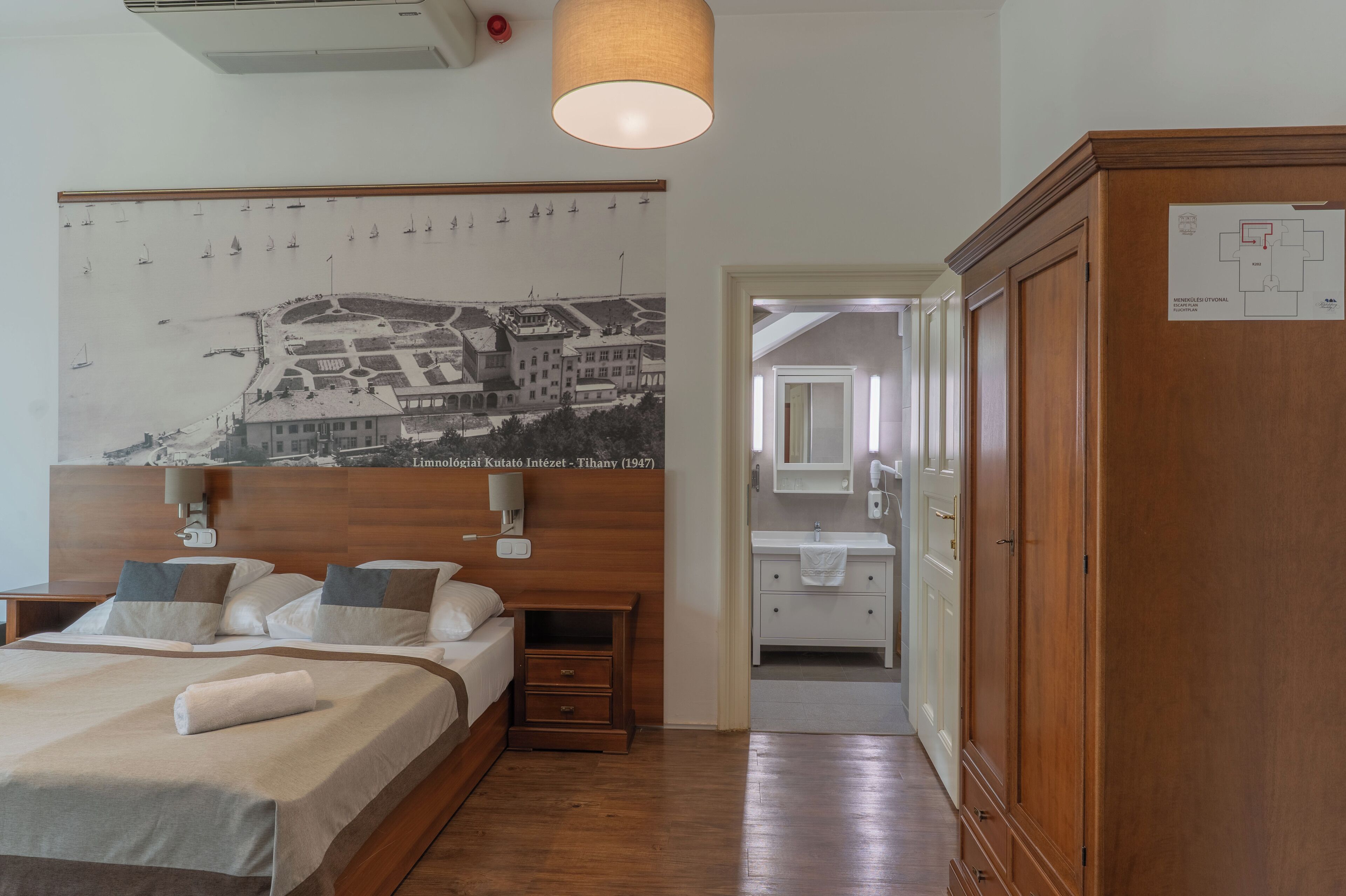 Habitación de hotel con una cama, un armario de madera, un baño con espejo y lavamanos, y una pared con un mapa histórico.