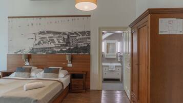 Habitación de hotel con una cama, un armario de madera, un baño con espejo y lavamanos, y una pared con un mapa histórico.