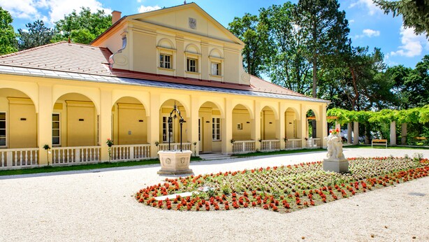 Un bâtiment de style classique, doté d’une façade symétrique, de fenêtres en arc de cercle et d’une cour intérieure où se trouvent une statue et des parterres de fleurs.
