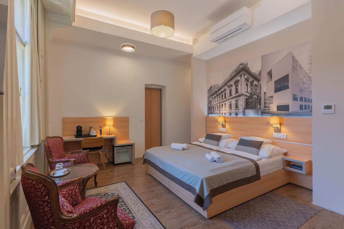 A hotel room with a bed, a desk, a chair, and a wall-mounted lamp.