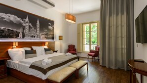 Une chambre d’hôtel avec un grand lit, une banquette, une chaise, un téléviseur et une fenêtre avec des rideaux.