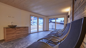 A waiting area with a wooden bench, a sink with a bowl, and large windows with a snowy mountain view.